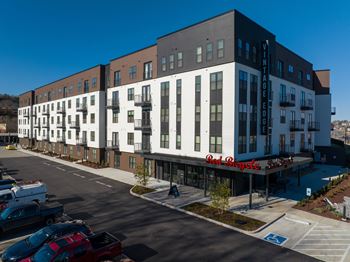 A modern multi-story building with a parking lot in front.